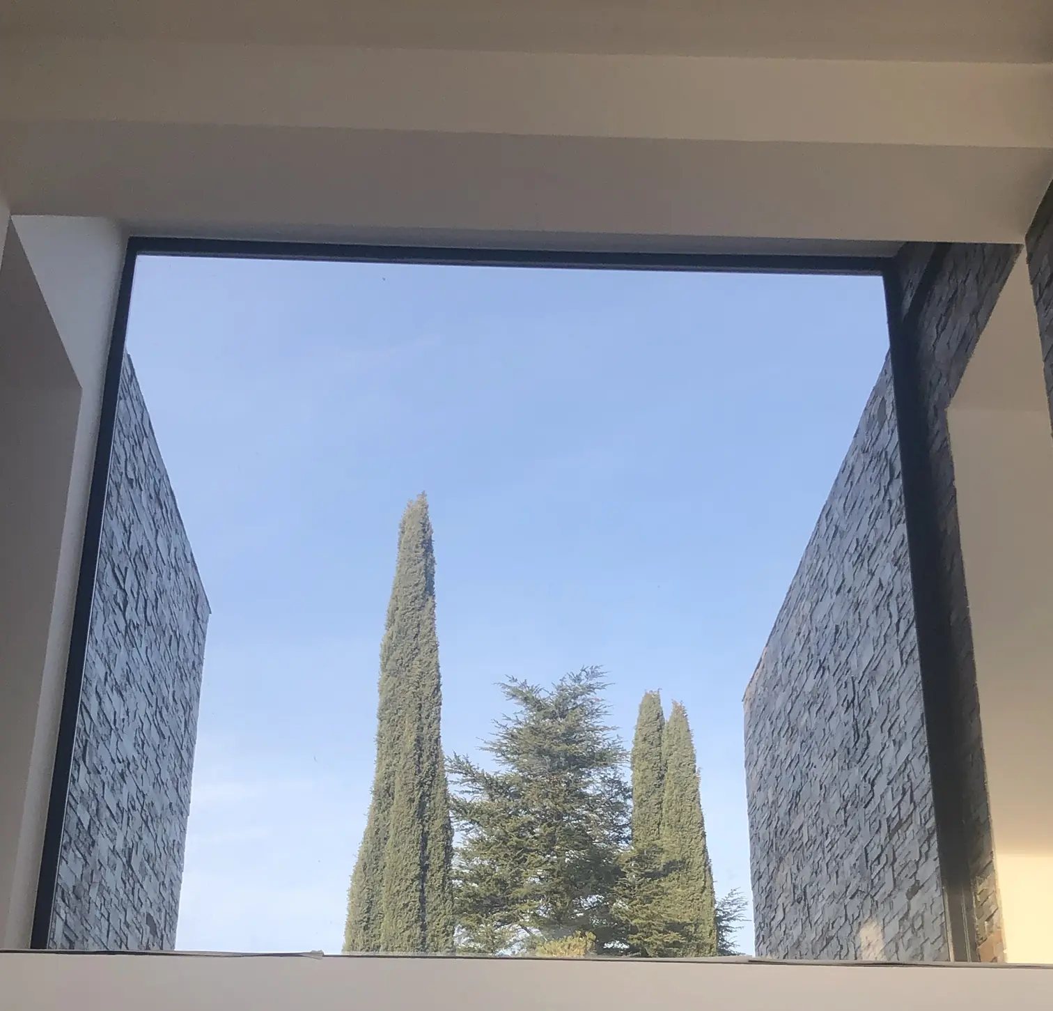 Gran ventanal que enmarca cipreses y cielo
