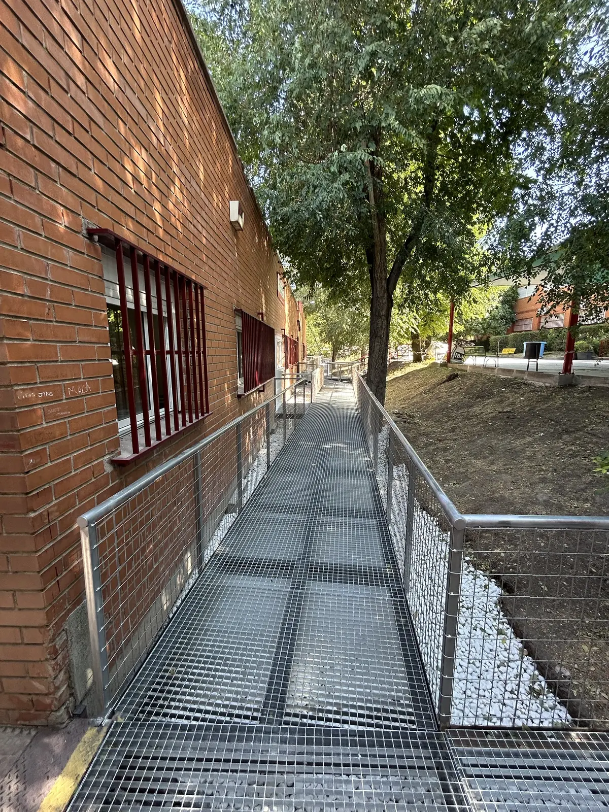 Rampa metálica junto a la fachada de ladrillo bajo los árboles